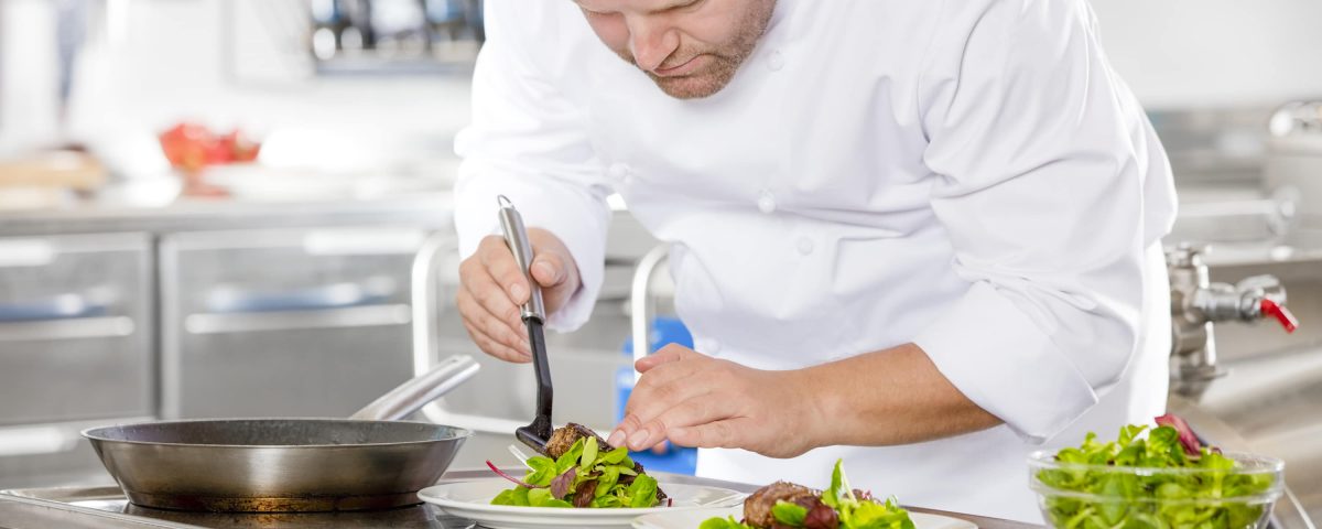 Cocinero preparando unos platos de ensalada y carne