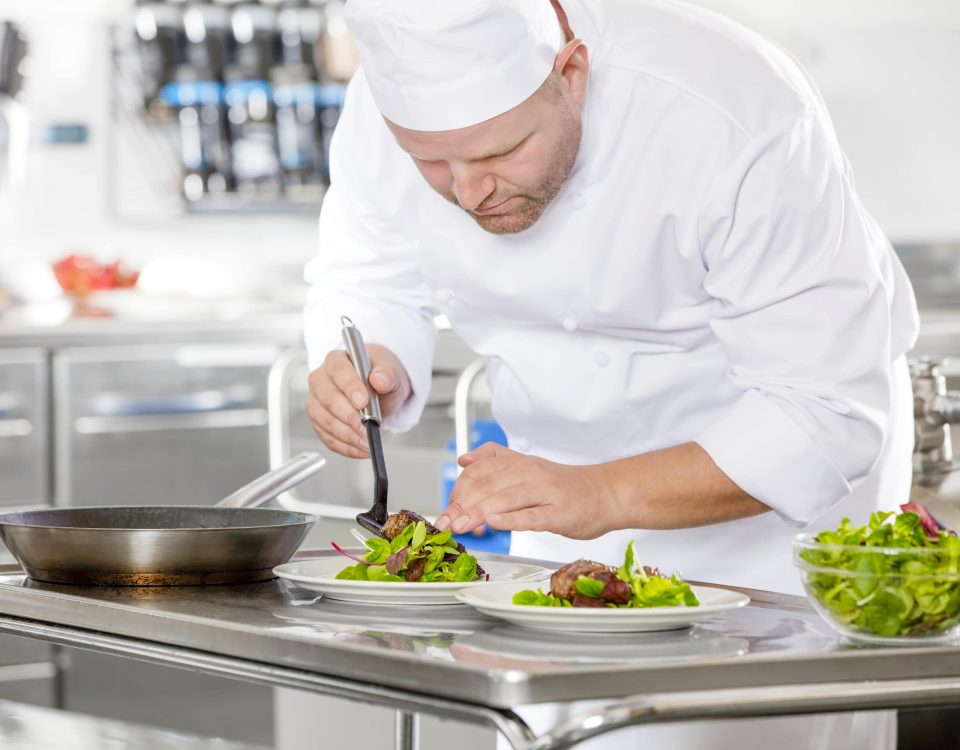 Cocinero preparando unos platos de ensalada y carne