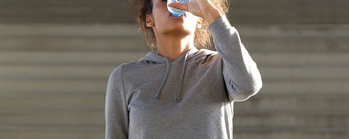 mujer vestida con ropa de deporte bebiendo agua en botella de plástico rellenada