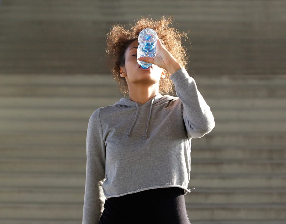 mujer vestida con ropa de deporte bebiendo agua en botella de plástico rellenada