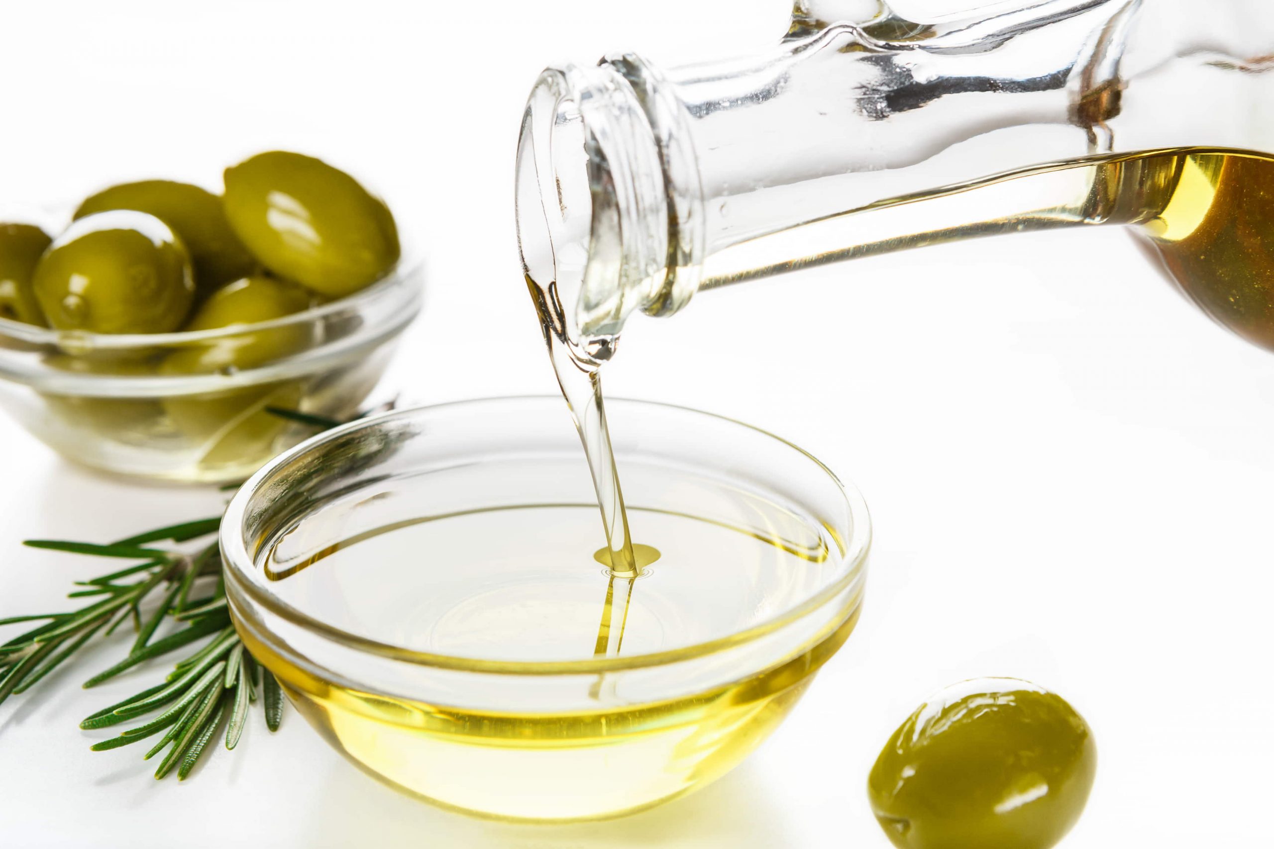 aceite de oliva echándolo en un cuenco pequeño y en otro lado tarro con aceitunas