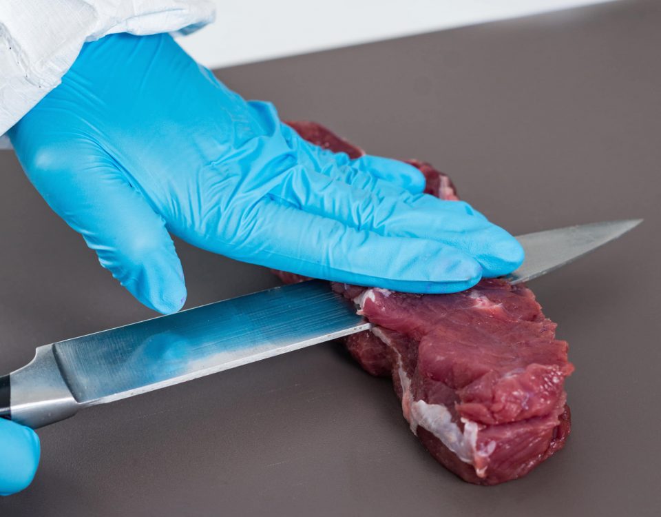 mano con un guante de color azul cortando carne con un cuchillo