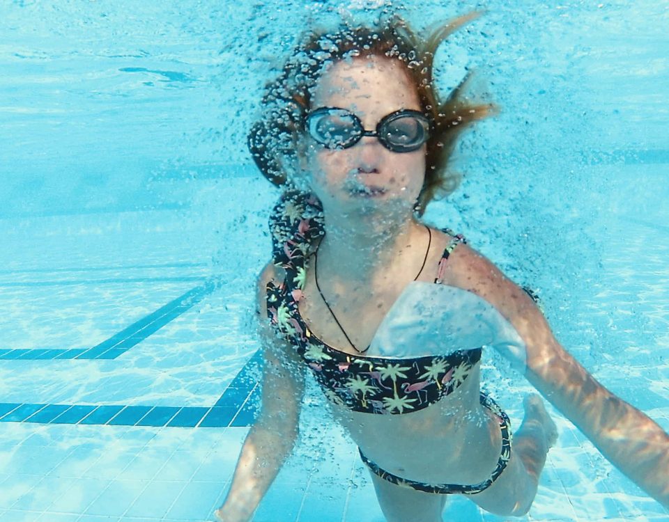 niña bajo agua con gafas de bucear para evitar la irritación de agua
