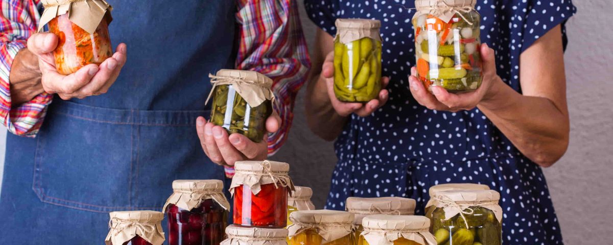 hombre y mujer mostrando tarros de comida que requieren conservación: pepinillos, melocotón, etc.