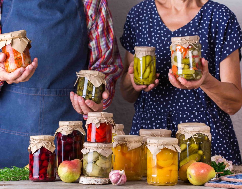 hombre y mujer mostrando tarros de comida que requieren conservación: pepinillos, melocotón, etc.